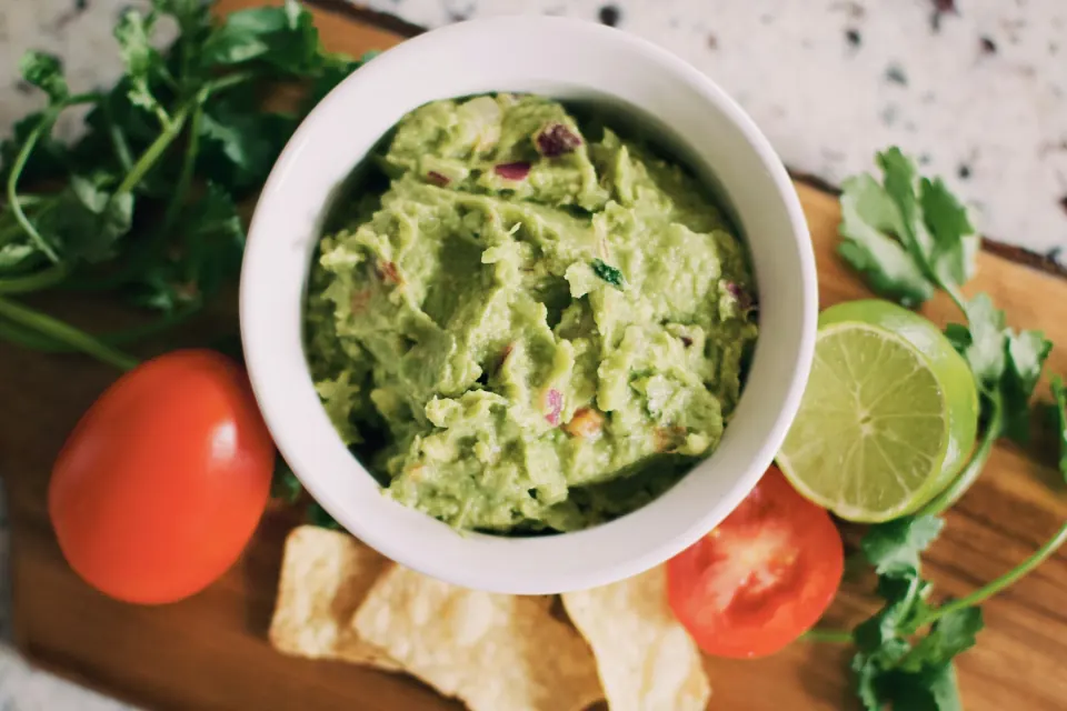 Beyaz kâsede guacamole, yanında lime ve cips